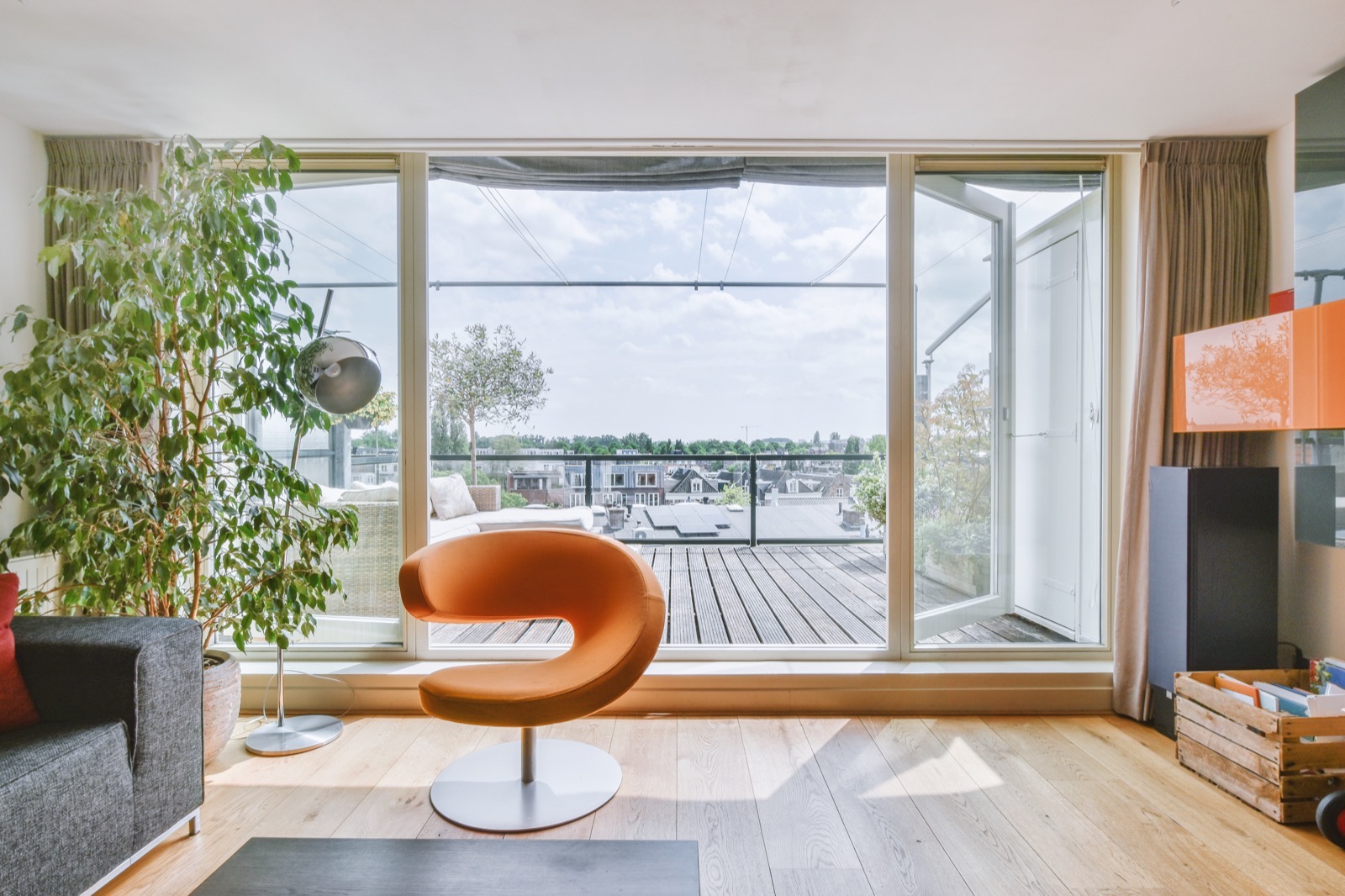 Lichte woonkamer van een appartement met een grote glazen pui naar een terras en de daken van de stad