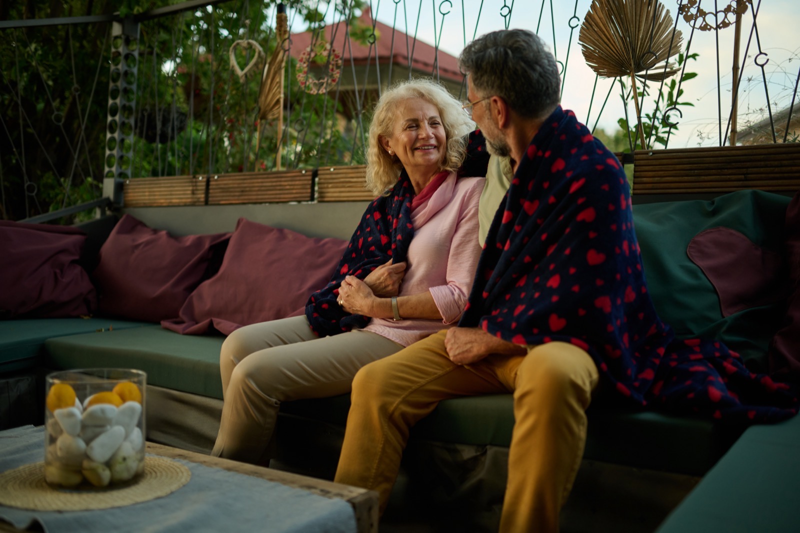 Een ouder koppel onder een plaid op het terras van een huis, aan het eind van het seizoen